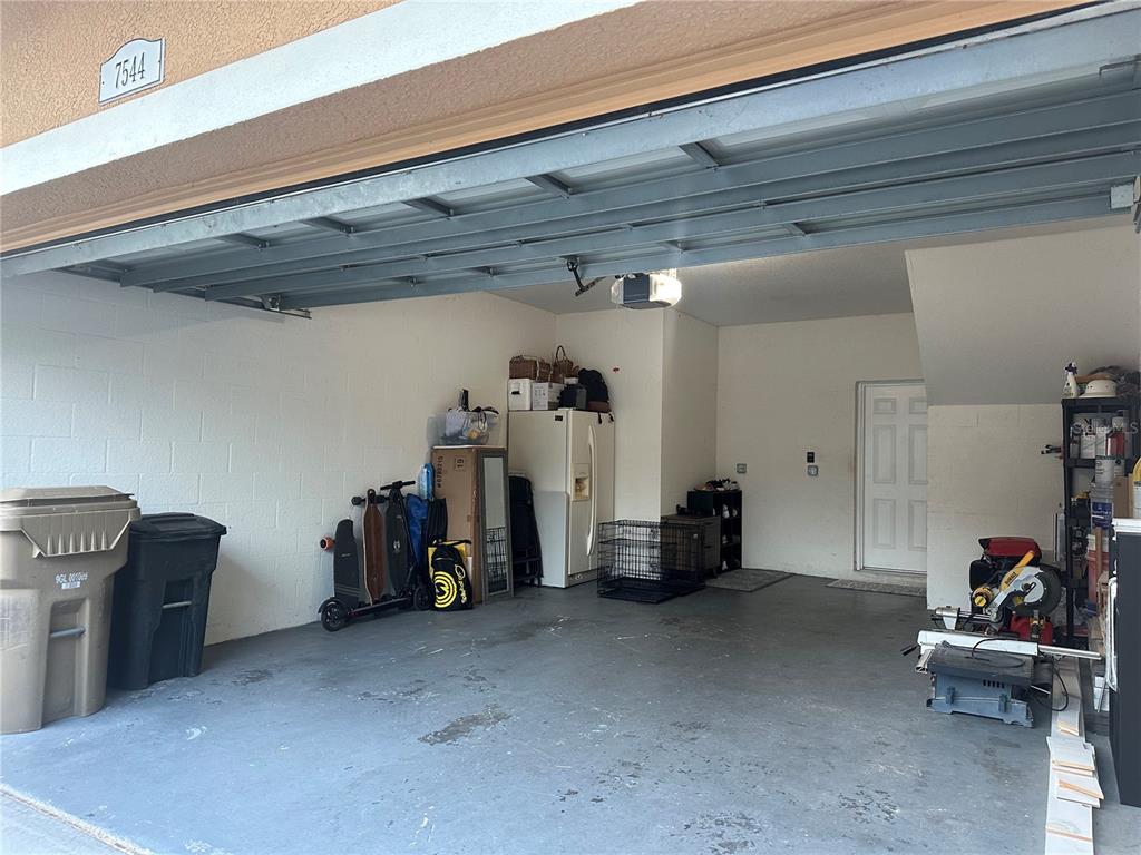 A garage with a concrete floor, a white refrigerator, storage items, and a door — 7544 RED MILL CIRCLE, NEW PORT RICHEY, FL
