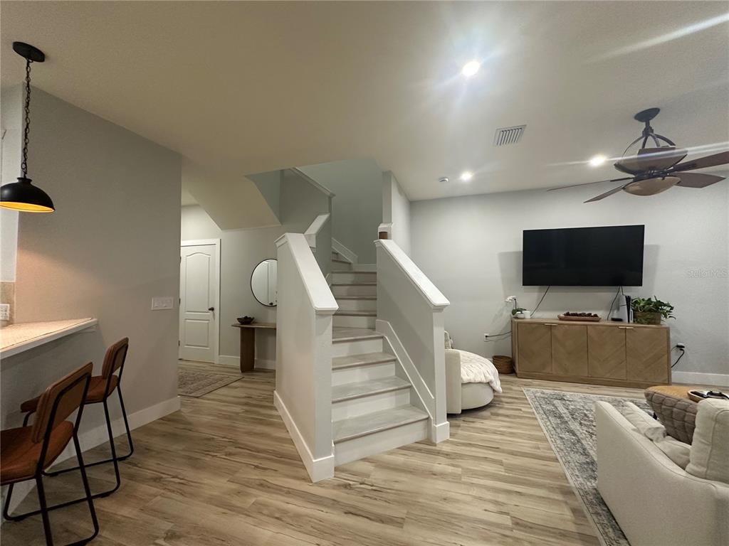 A living room features light wood flooring, a central staircase, and a wall-mounted television — 7544 RED MILL CIRCLE, NEW PORT RICHEY, FL