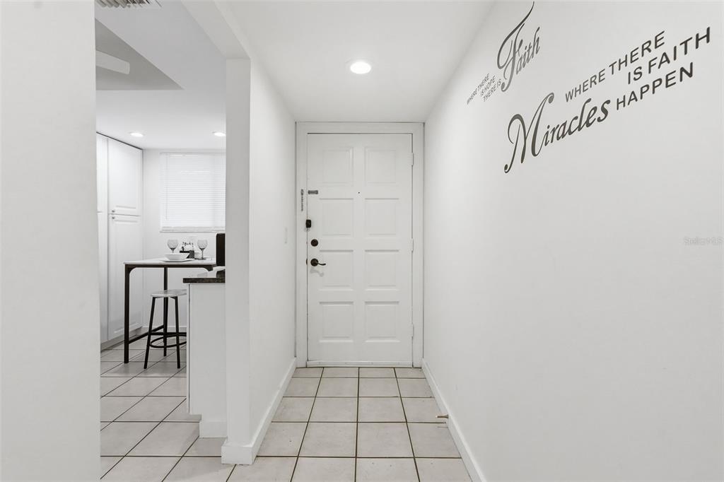 A white entryway with tiled floors leads to a front door and an adjacent kitchen — 6340 NEWTOWN CIRCLE UNIT 40A2, TAMPA, FL