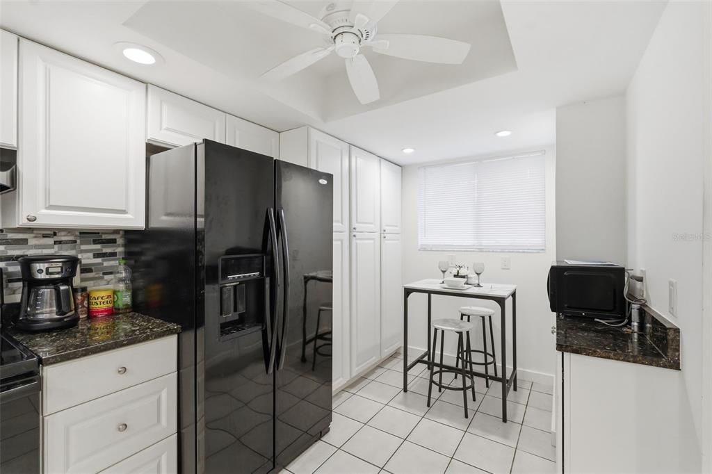 A kitchen features white cabinetry, black appliances, dark granite countertops, and a small dining table — 6340 NEWTOWN CIRCLE UNIT 40A2, TAMPA, FL