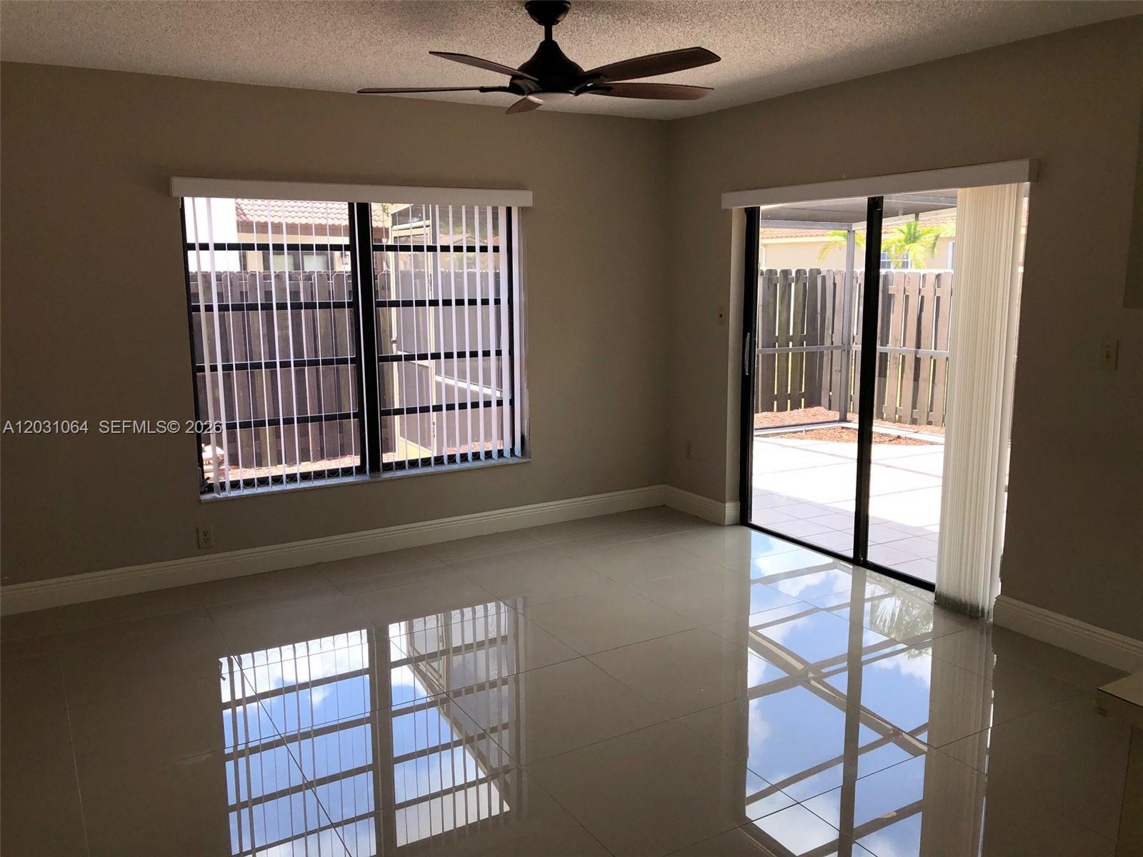An empty room features glossy tile flooring, a ceiling fan, vertical blinds, and sliding glass doors — 9082 SW 112 PL, Miami FL 33176, MIAMI, FL