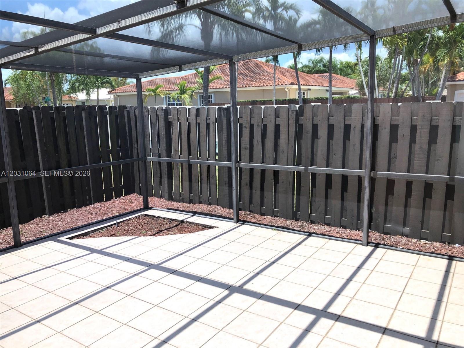 A screened-in patio features light-colored floor tiles, a dark wooden fence, and a small garden bed — 9082 SW 112 PL, Miami FL 33176, MIAMI, FL