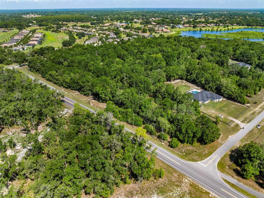 An aerial view shows a wooded lot bordered by a road and nearby residential homes — Lot 1 HOJIN STREET, SORRENTO, FL