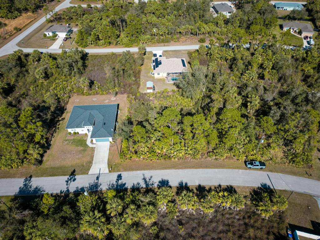 An aerial view shows two houses surrounded by dense woods and a paved road — BELCHER AVENUE, NORTH PORT, FL