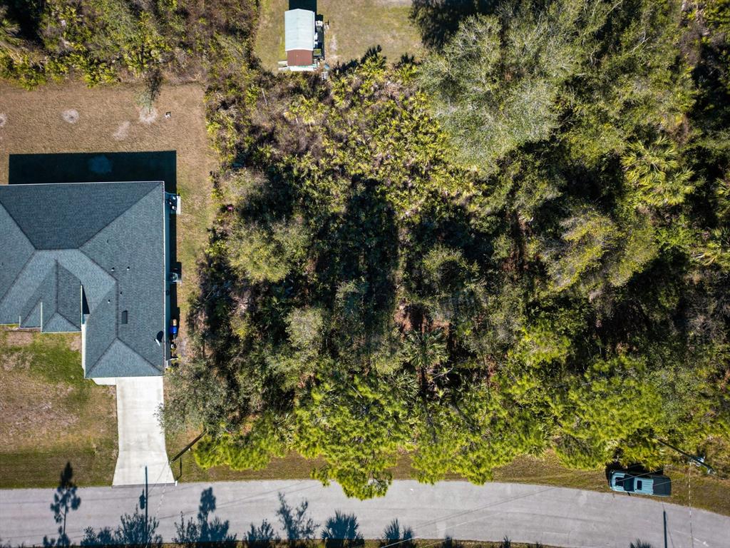 An aerial view shows a house with a driveway next to a wooded vacant lot — BELCHER AVENUE, NORTH PORT, FL