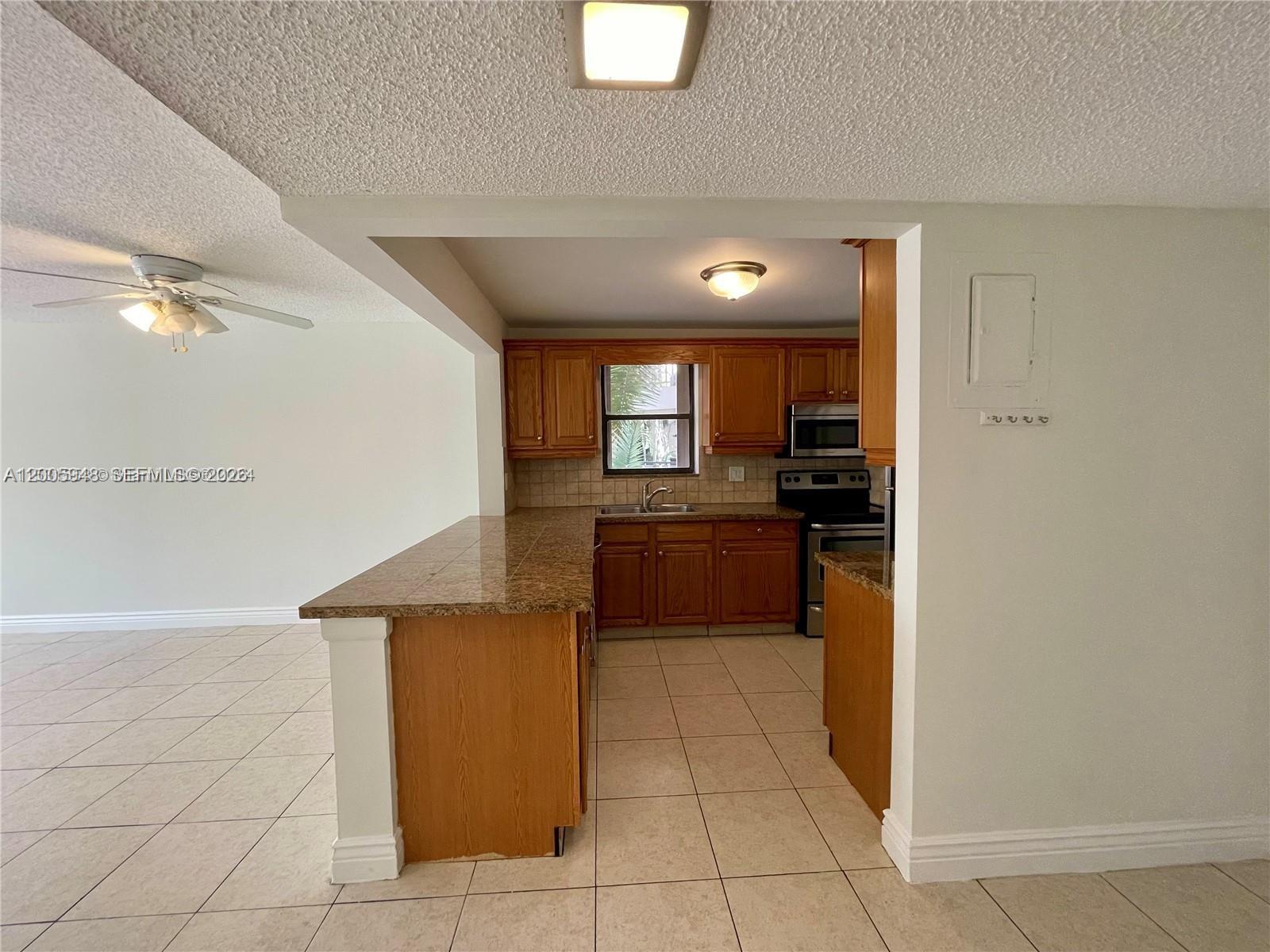 A kitchen with wood cabinets and granite countertops opens to a tiled living area — 2320 S Cypress Bend Dr # 204, Pompano Beach FL 33069, POMPANO BEACH, FL
