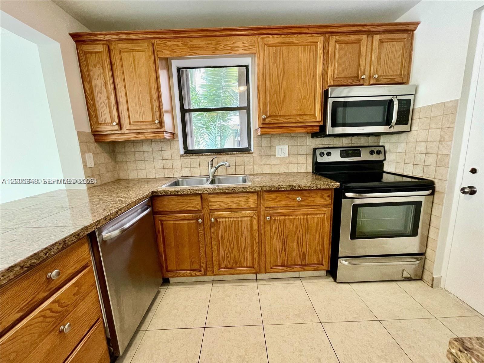 A kitchen features wood cabinets, granite countertops, stainless steel appliances, and a tiled backsplash — 2320 S Cypress Bend Dr # 204, Pompano Beach FL 33069, POMPANO BEACH, FL