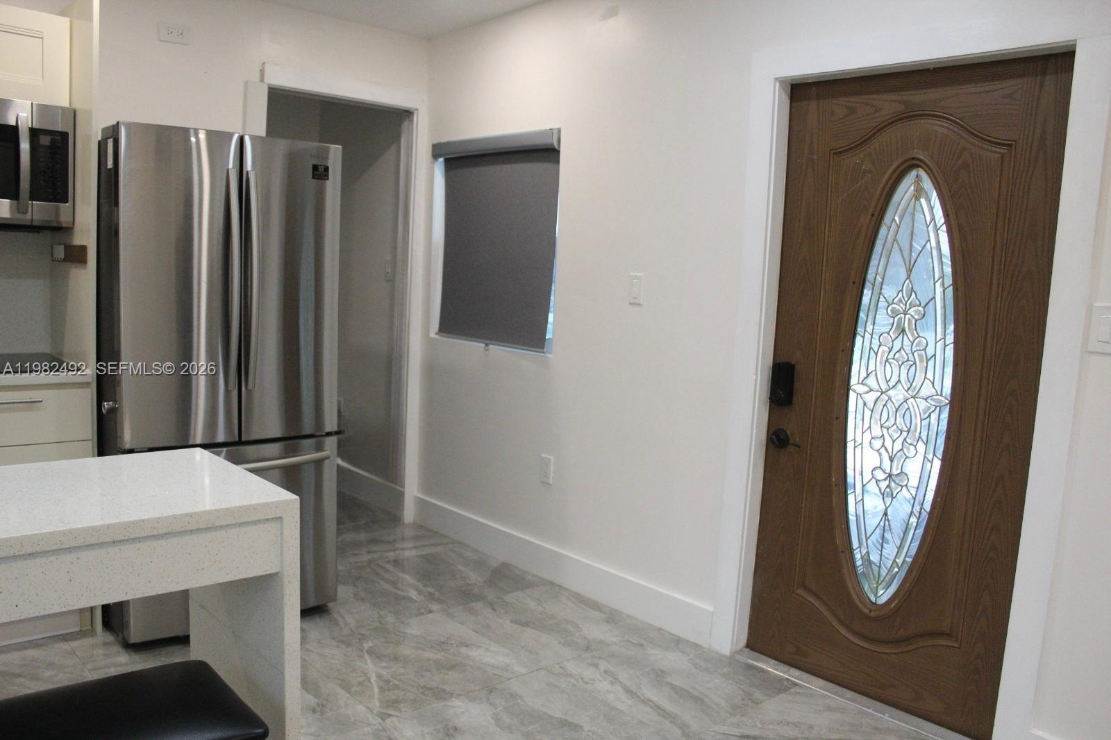 A kitchen features stainless steel appliances, a white island, and a wooden front door — 115 SW 115th Ave, Miramar FL 33025, MIRAMAR, FL