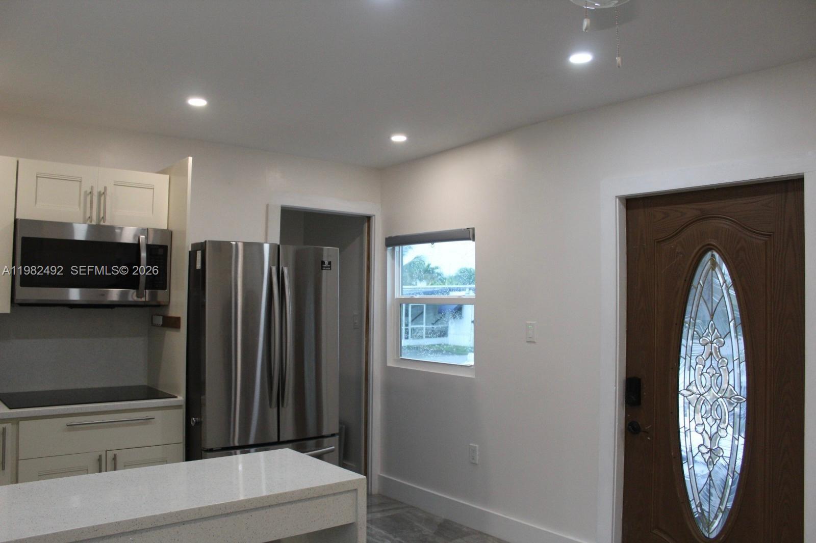 A kitchen features white cabinets, stainless steel appliances, a quartz island, and a wooden door — 115 SW 115th Ave, Miramar FL 33025, MIRAMAR, FL