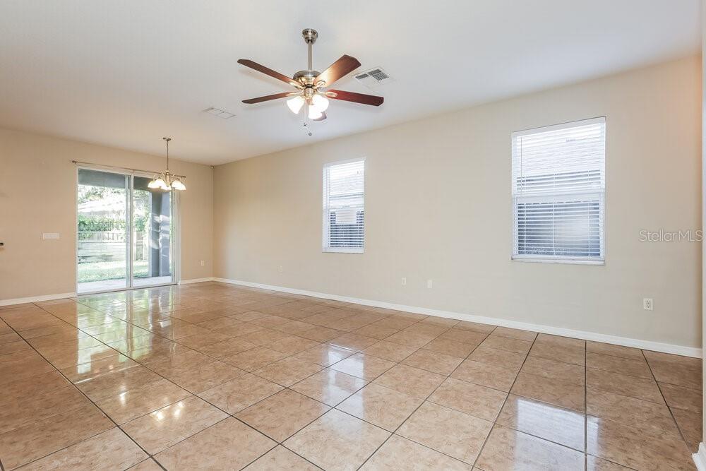 An empty living room features beige walls, tile flooring, a ceiling fan, and sliding glass doors — 11813 MANGO GROVES BOULEVARD, SEFFNER, FL