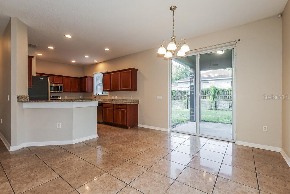 A kitchen with wood cabinets and tile floors opens to a dining area with sliding doors — 11813 MANGO GROVES BOULEVARD, SEFFNER, FL