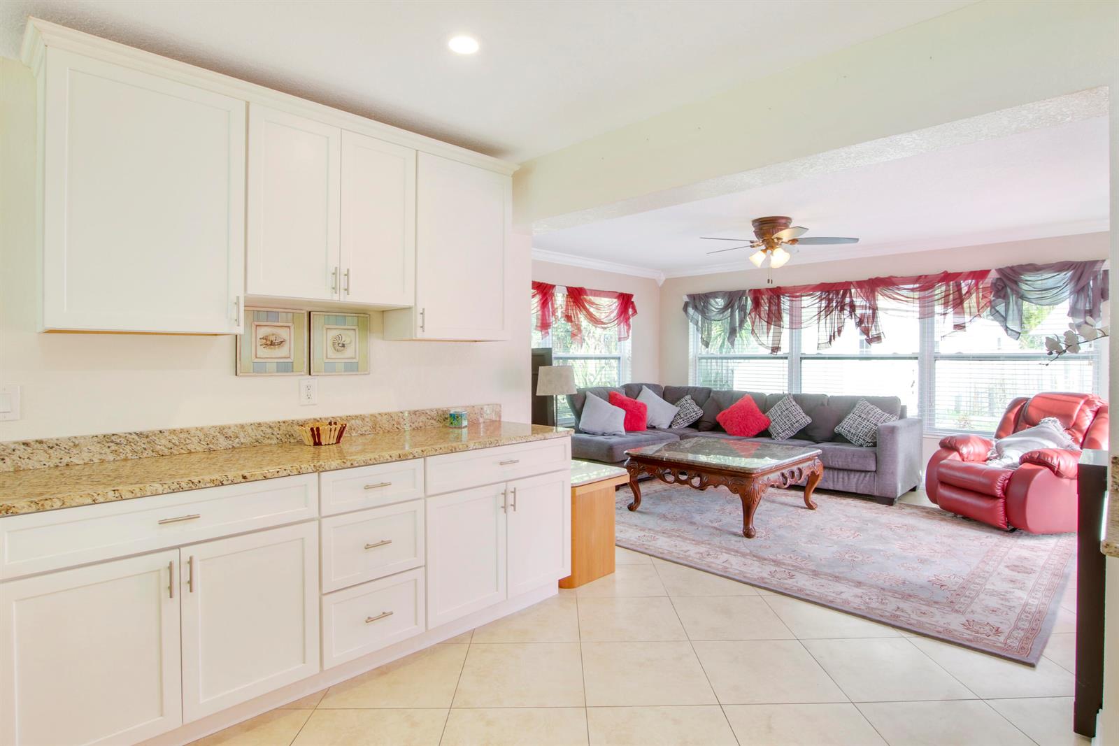 A kitchen with white cabinets and granite countertops opens into a living room with furniture — 19185 SE Homewood Avenue, Jupiter FL 33469, JUPITER, FL