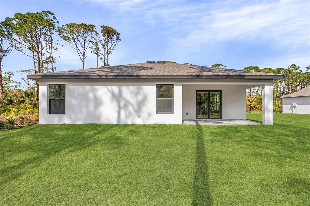 The back exterior of a white house features a covered patio and a grassy yard — 4081 LONGWELL LANE, NORTH PORT, FL