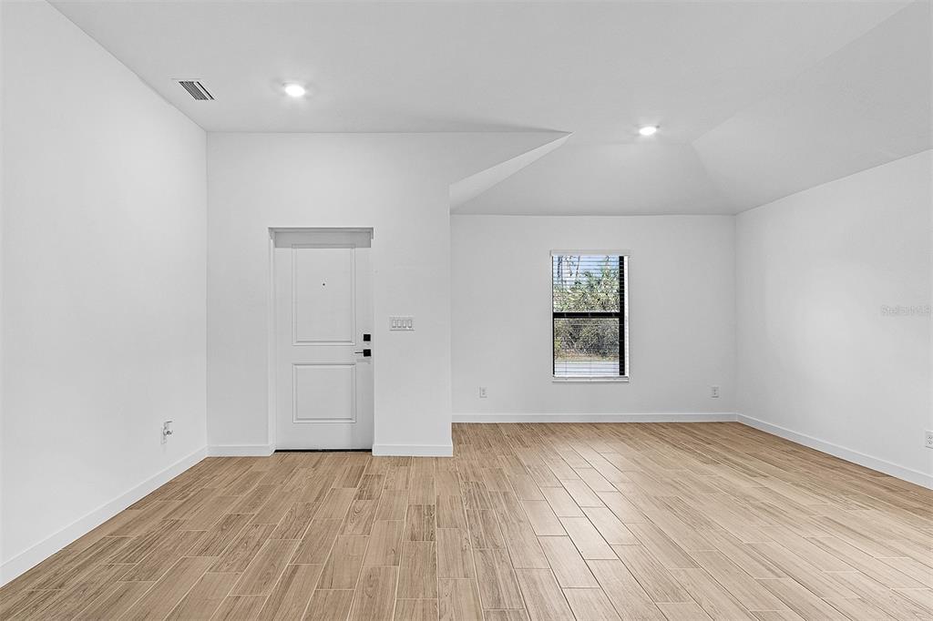 An empty room with white walls, light wood-look flooring, a front door, and a window — 4081 LONGWELL LANE, NORTH PORT, FL
