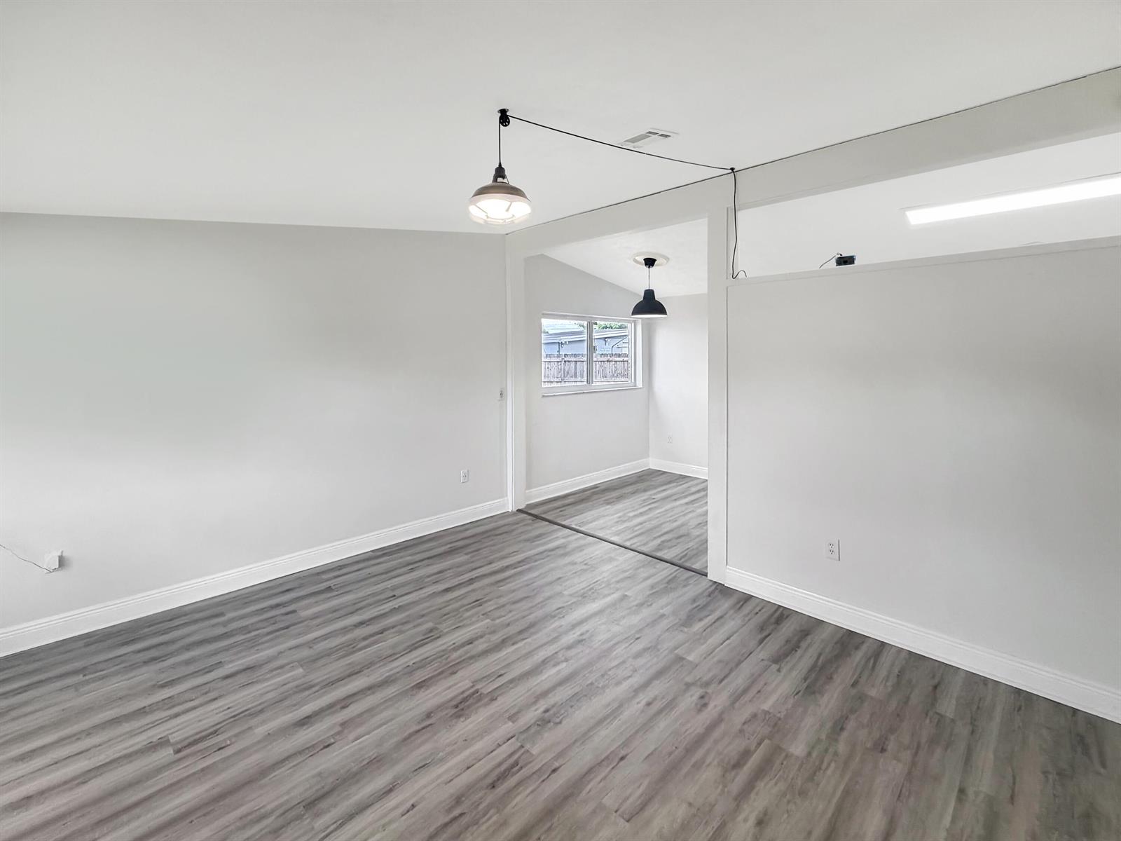 An empty room with gray wood-look flooring, white walls, and two hanging pendant lights — 752 Orchid Drive, Royal Palm Beach FL 33411, ROYAL PALM BEACH, FL