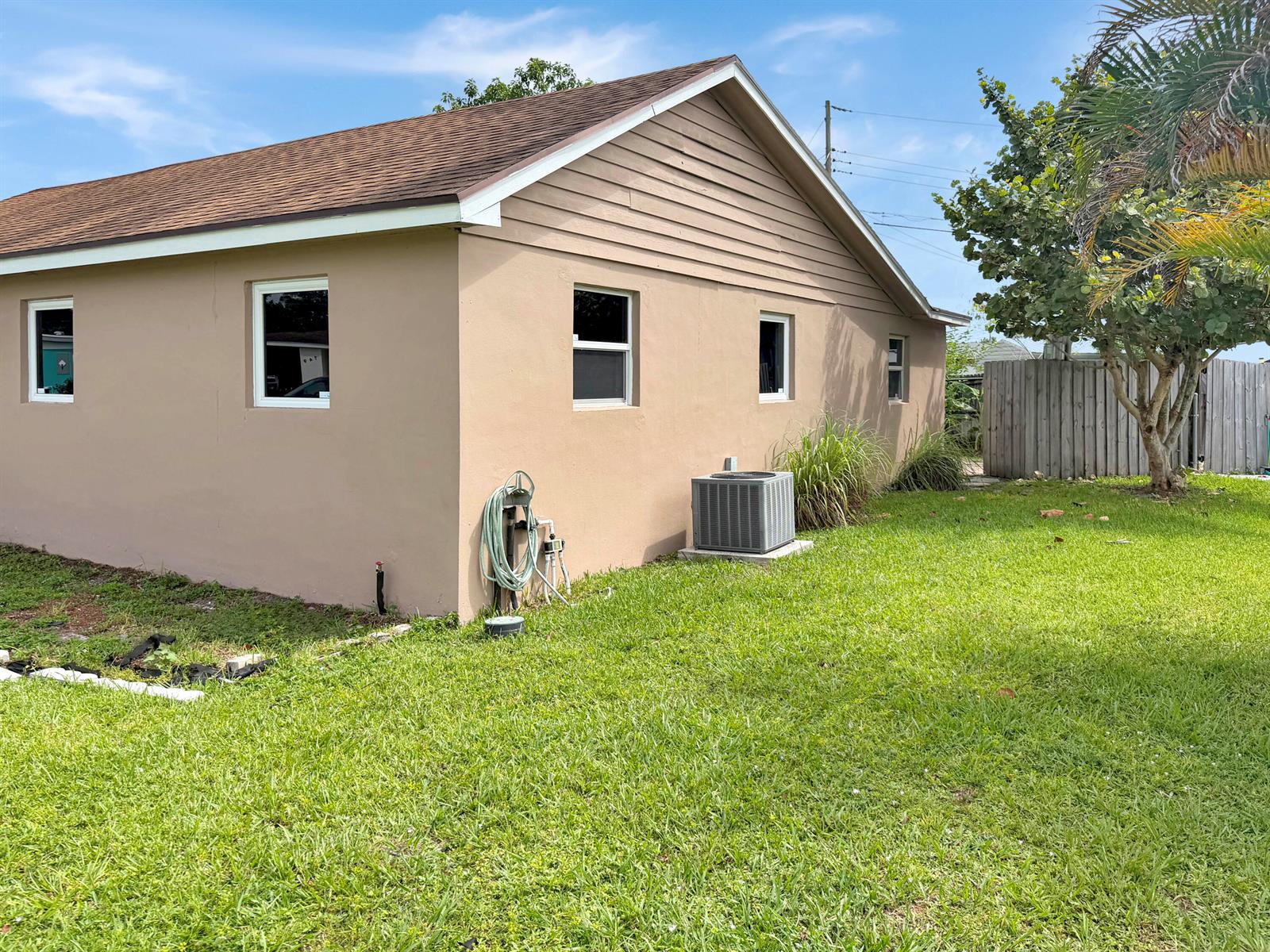 The exterior of a tan, single-story house features a brown shingled roof and air conditioner — 752 Orchid Drive, Royal Palm Beach FL 33411, ROYAL PALM BEACH, FL