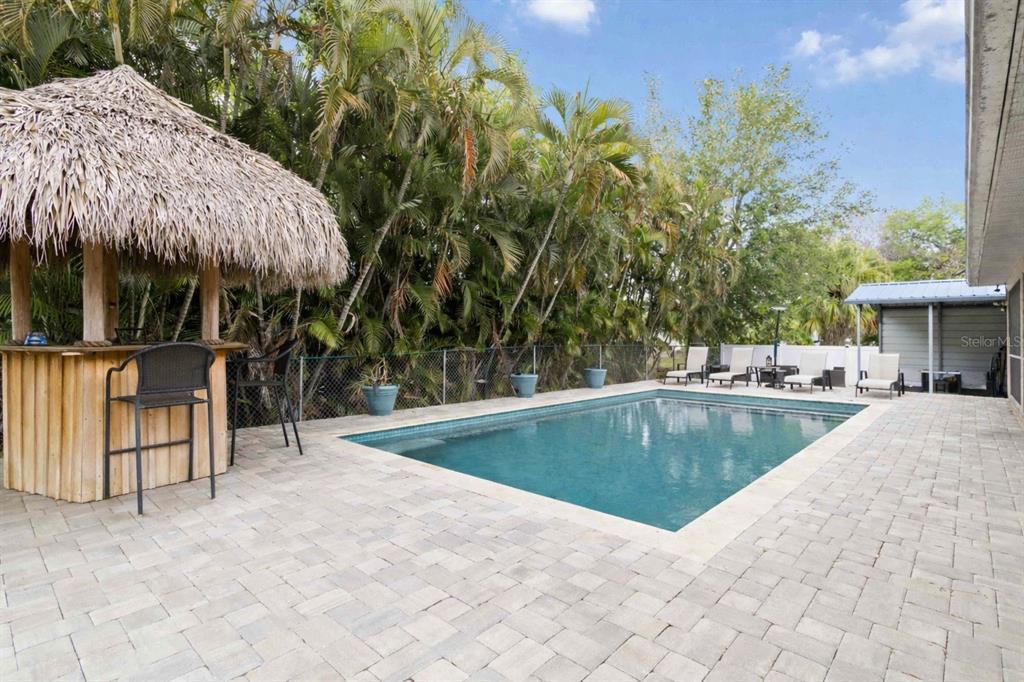 A swimming pool sits in front of a chain-link fence and lush palm trees — 807 IXORA AVENUE, ELLENTON, FL