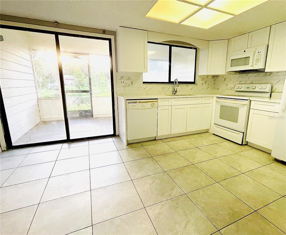 A kitchen with white cabinets, white appliances, tile flooring, and a sliding glass door — 1420 RIDGE LAKE COURT, LAKELAND, FL