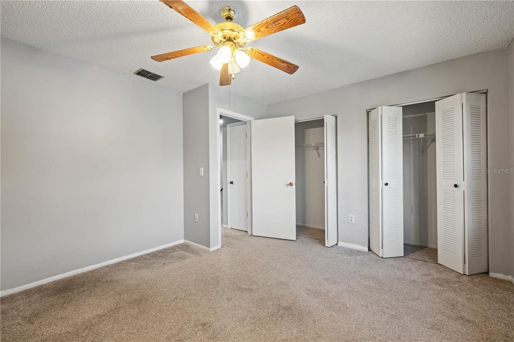 A bedroom with gray walls, beige carpet, a ceiling fan, and two open closet doors — 1420 RIDGE LAKE COURT, LAKELAND, FL