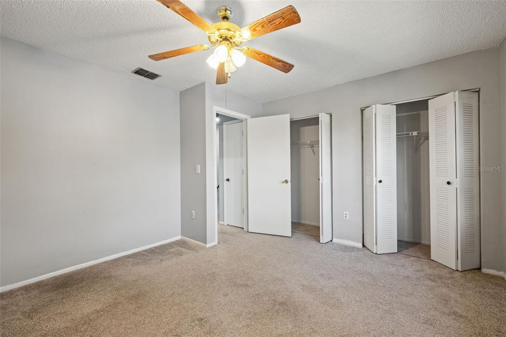 A bedroom with gray walls, beige carpet, a ceiling fan, and two open closet doors — 1420 RIDGE LAKE COURT, LAKELAND, FL