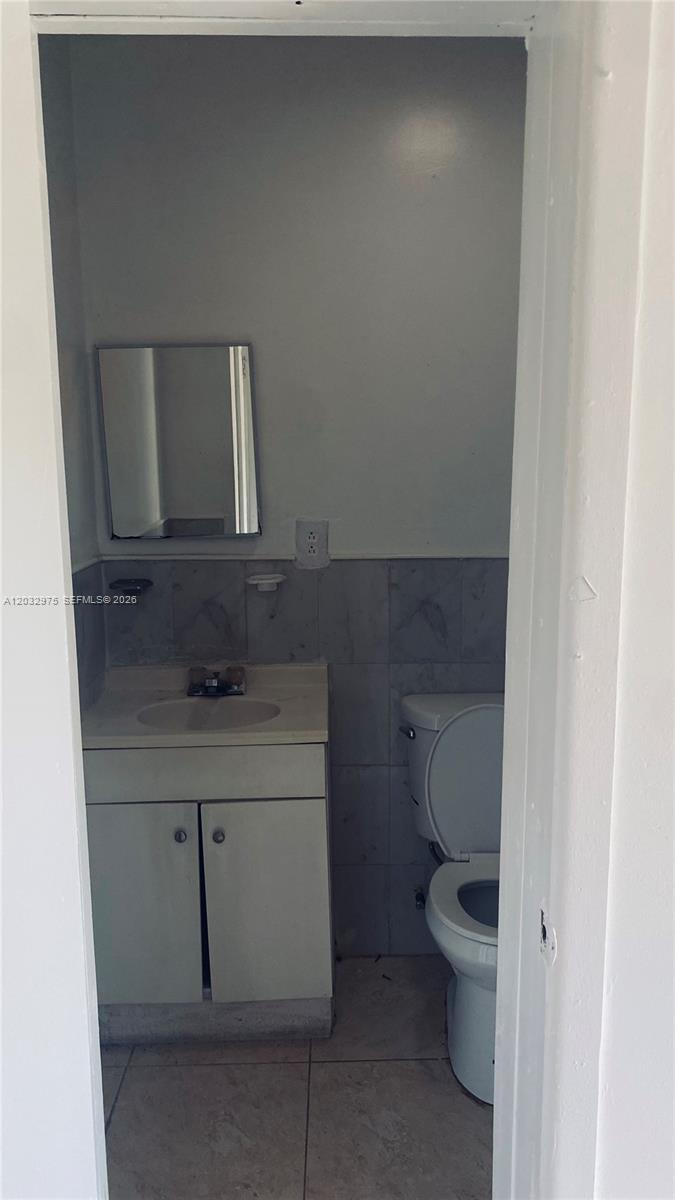 A small bathroom features a vanity with a sink, a toilet, and tiled walls — 1070 NW 147th St # 0, Miami FL 33168, MIAMI, FL