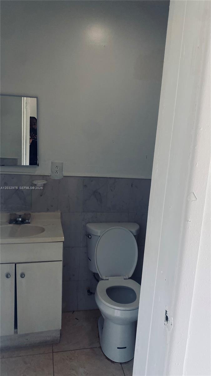 A small bathroom features a white vanity, a toilet, and light-colored wall tiles — 1070 NW 147th St # 0, Miami FL 33168, MIAMI, FL