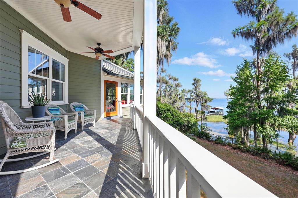 A covered porch with slate tile flooring overlooks a lake with trees and a dock — 23014 NE 69TH AVENUE, MELROSE, FL