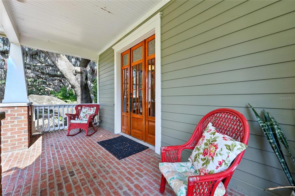 A covered porch with a brick floor, two red wicker chairs, and wooden double doors — 23014 NE 69TH AVENUE, MELROSE, FL