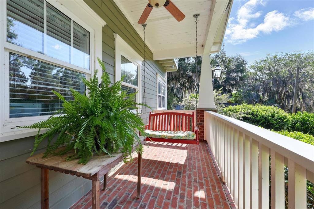 A covered porch features a red hanging bench, a potted fern, and brick flooring — 23014 NE 69TH AVENUE, MELROSE, FL
