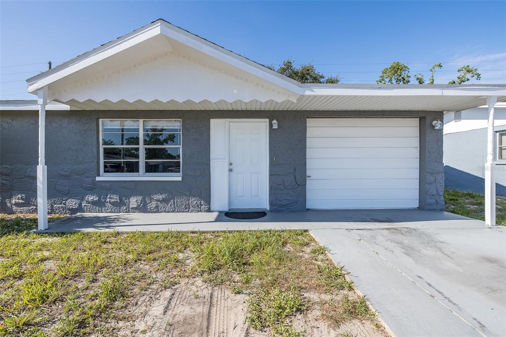 A single-story house with a gray stucco exterior, a white front door, and a garage — 7734 COVENTRY DRIVE, PORT RICHEY, FL