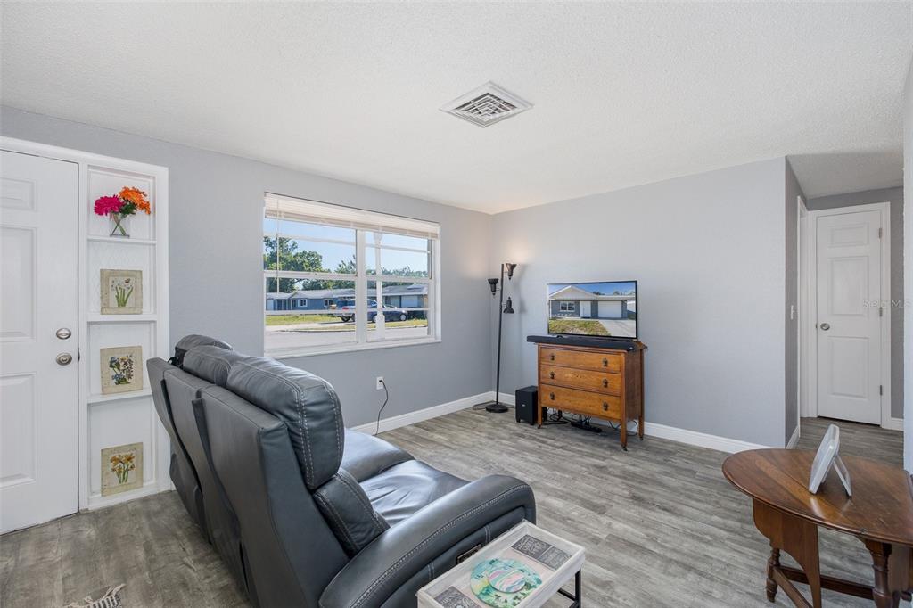 A living room with gray walls, wood-look flooring, a gray sofa, and a television stand — 7734 COVENTRY DRIVE, PORT RICHEY, FL