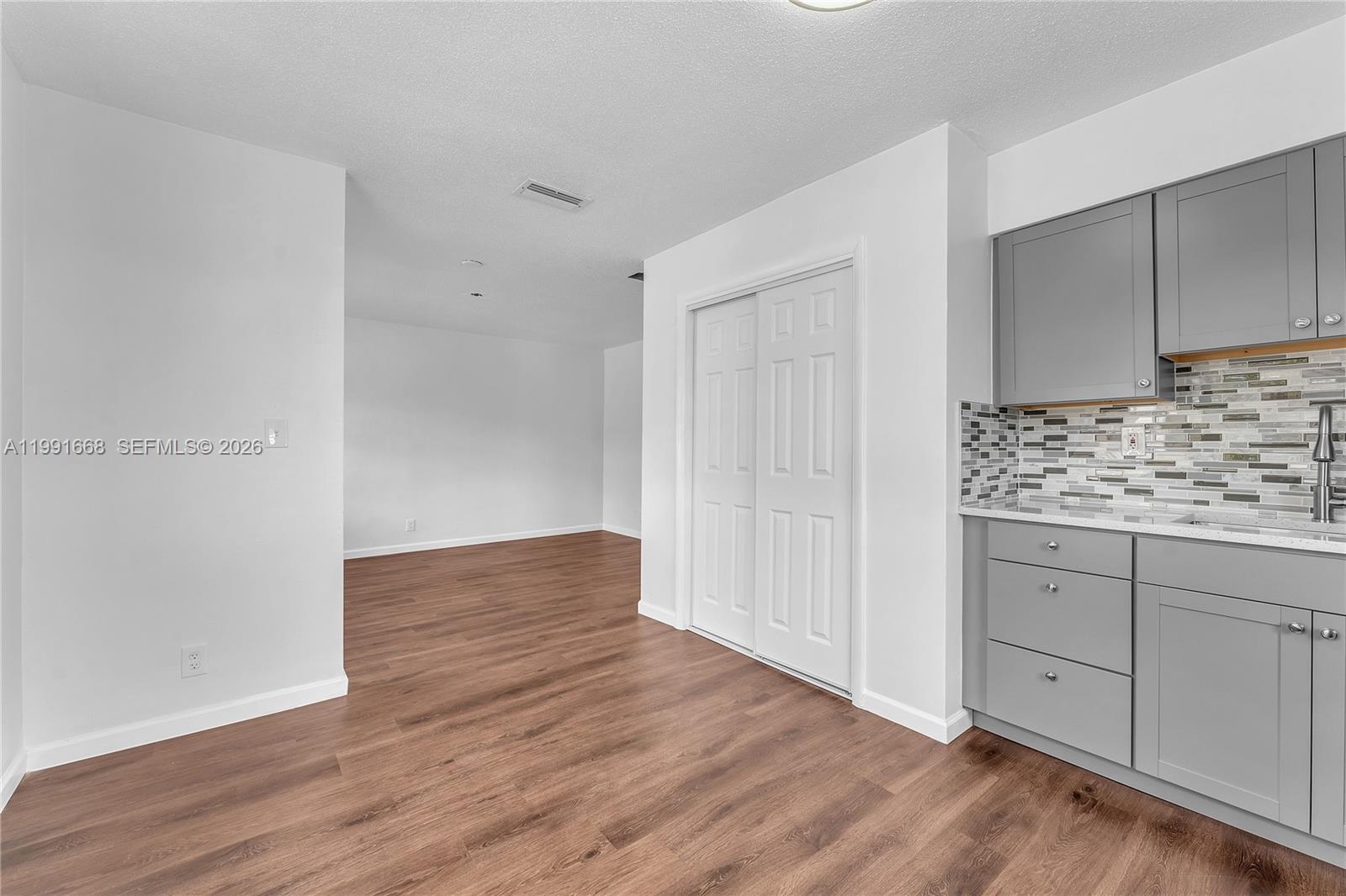 A kitchen area with gray cabinets and a tiled backsplash opens into a living space — 3750 SW 59th Ave # 3, Davie FL 33314, DAVIE, FL