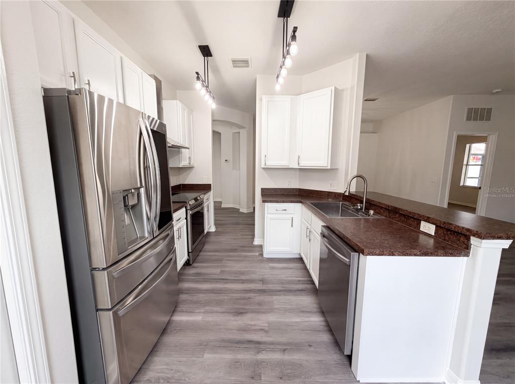 A kitchen features white cabinets, dark countertops, stainless steel appliances, and wood-look flooring — 3408 GROVE BLOSSOM LANE, PLANT CITY, FL
