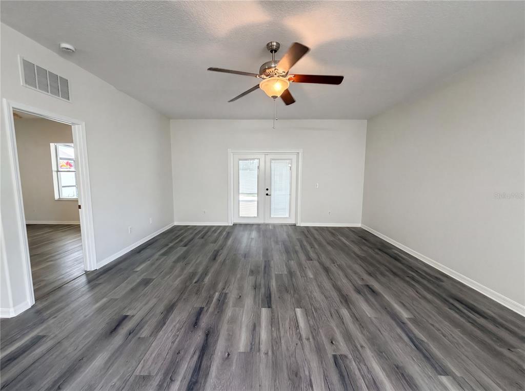 An empty room features gray wood-look flooring, a ceiling fan, and white French doors — 3408 GROVE BLOSSOM LANE, PLANT CITY, FL