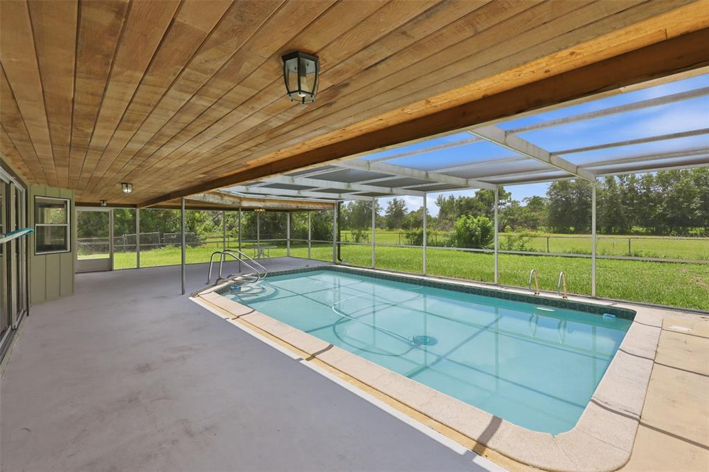 A covered patio with outdoor furniture overlooks a screened-in swimming pool and a grassy yard — 4475 CYPRESS COUNTRY LANE, LAKELAND, FL