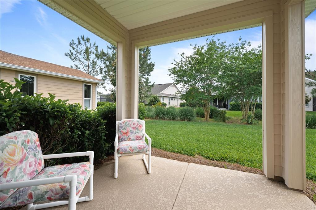 A covered patio features two floral-patterned chairs overlooking a grassy backyard and neighboring houses — 5610 NW 37TH LANE ROAD, OCALA, FL