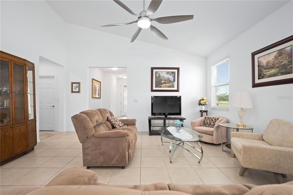 A living room features tile flooring, a vaulted ceiling with a fan, and neutral furniture — 5610 NW 37TH LANE ROAD, OCALA, FL