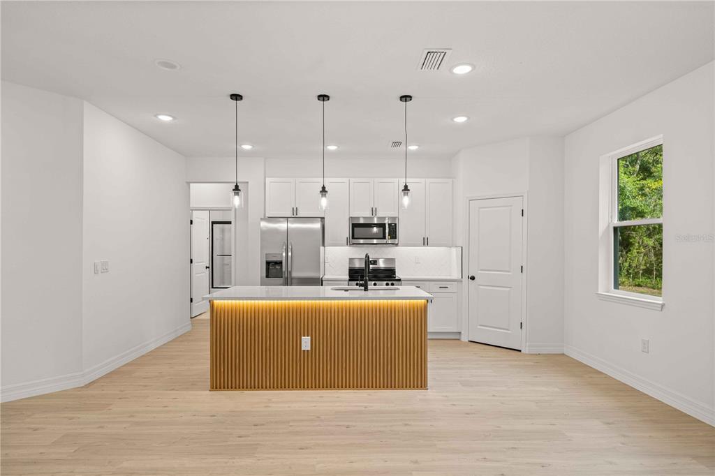A modern kitchen features white cabinetry, a stainless steel refrigerator, and a slatted wood island — 1197 W G MARTINELLI BOULEVARD, CITRUS SPRINGS, FL