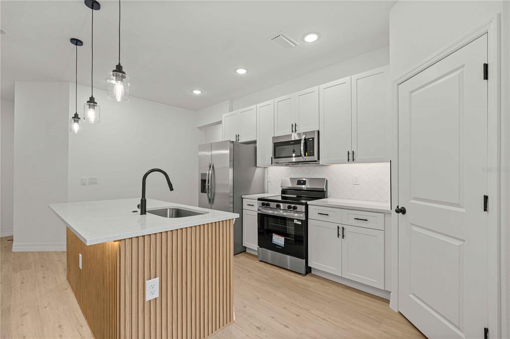 A modern kitchen features white cabinetry, stainless steel appliances, and a wood-slatted kitchen island — 1197 W G MARTINELLI BOULEVARD, CITRUS SPRINGS, FL