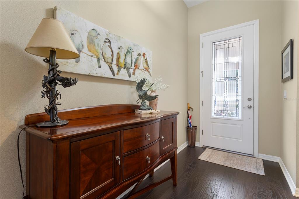 An entryway features a wooden sideboard, a bird-themed painting, a table lamp, and a front door — 2651 PEONY DRIVE, OVIEDO, FL