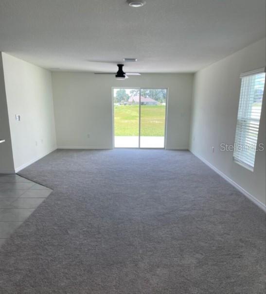 An open-concept living area features beige carpeting, a kitchen island, and a ceiling fan — 6484 SE 4TH LANE, OCALA, FL