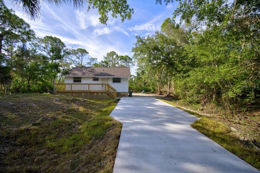 A white house with a wooden deck sits at the end of a concrete driveway — 28060 CHRYSALIS DRIVE, PUNTA GORDA, FL