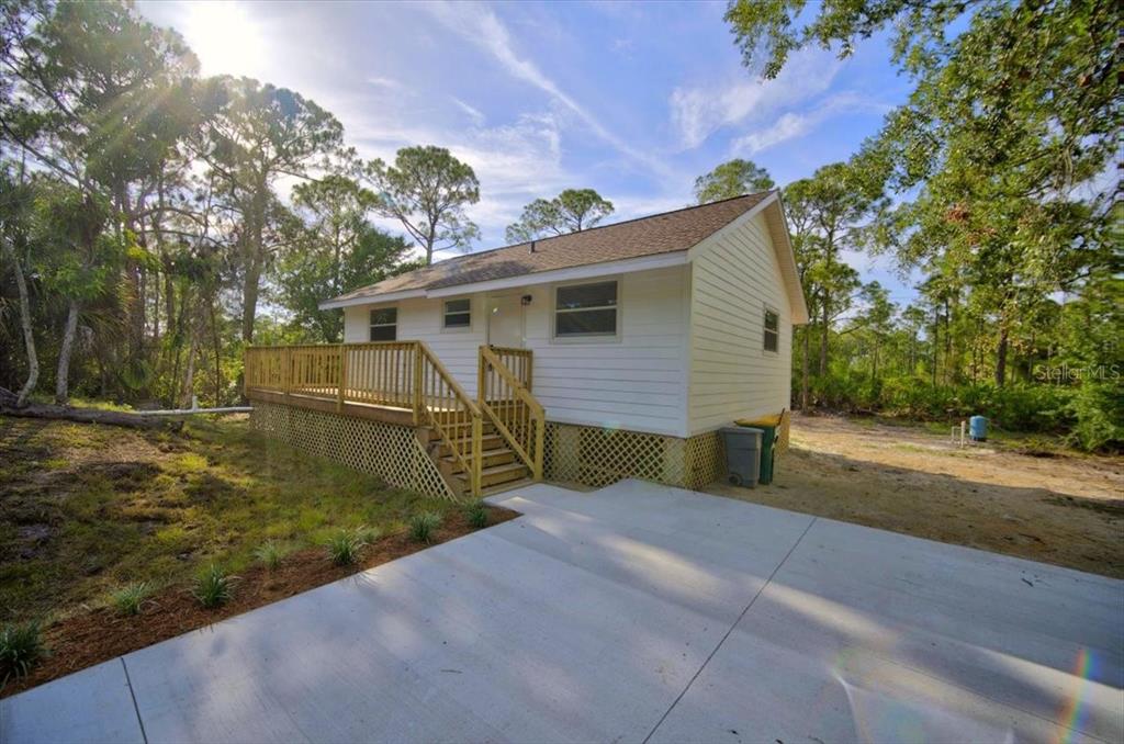 A white house with a wooden deck and stairs sits next to a concrete driveway — 28060 CHRYSALIS DRIVE, PUNTA GORDA, FL