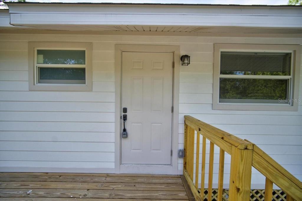 A white exterior wall features a six-panel door, two windows, and a wooden deck railing — 28060 CHRYSALIS DRIVE, PUNTA GORDA, FL