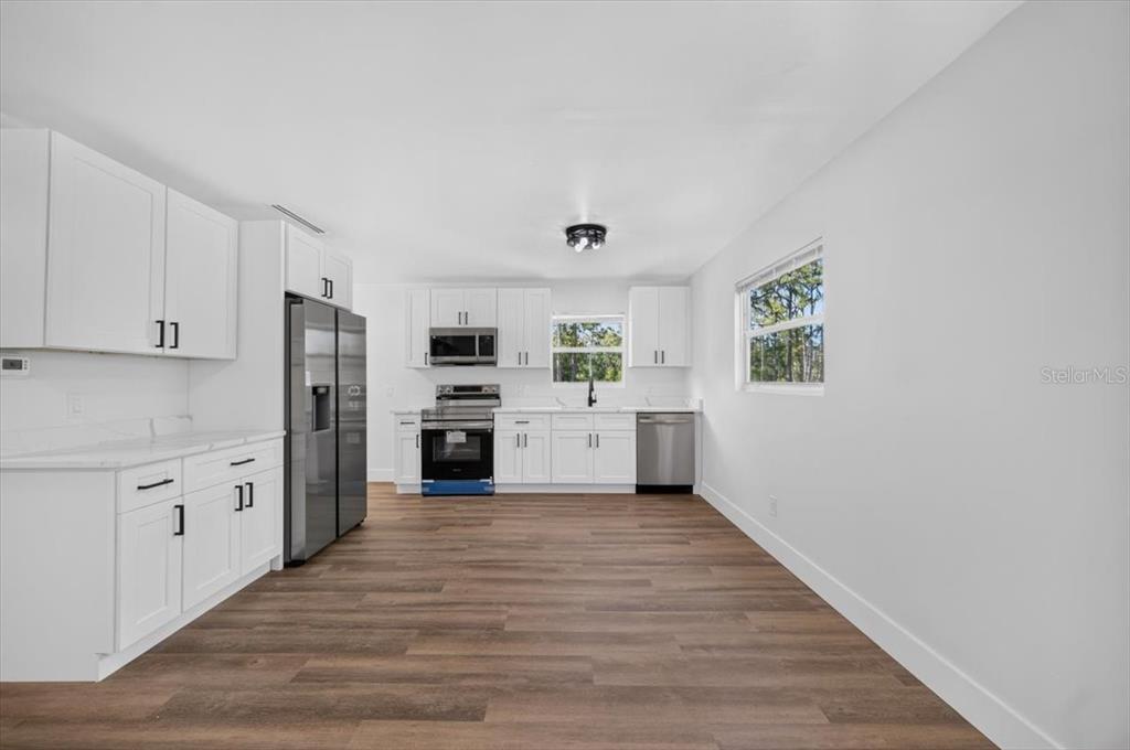A kitchen features white cabinets, stainless steel appliances, and wood-look flooring — 28060 CHRYSALIS DRIVE, PUNTA GORDA, FL
