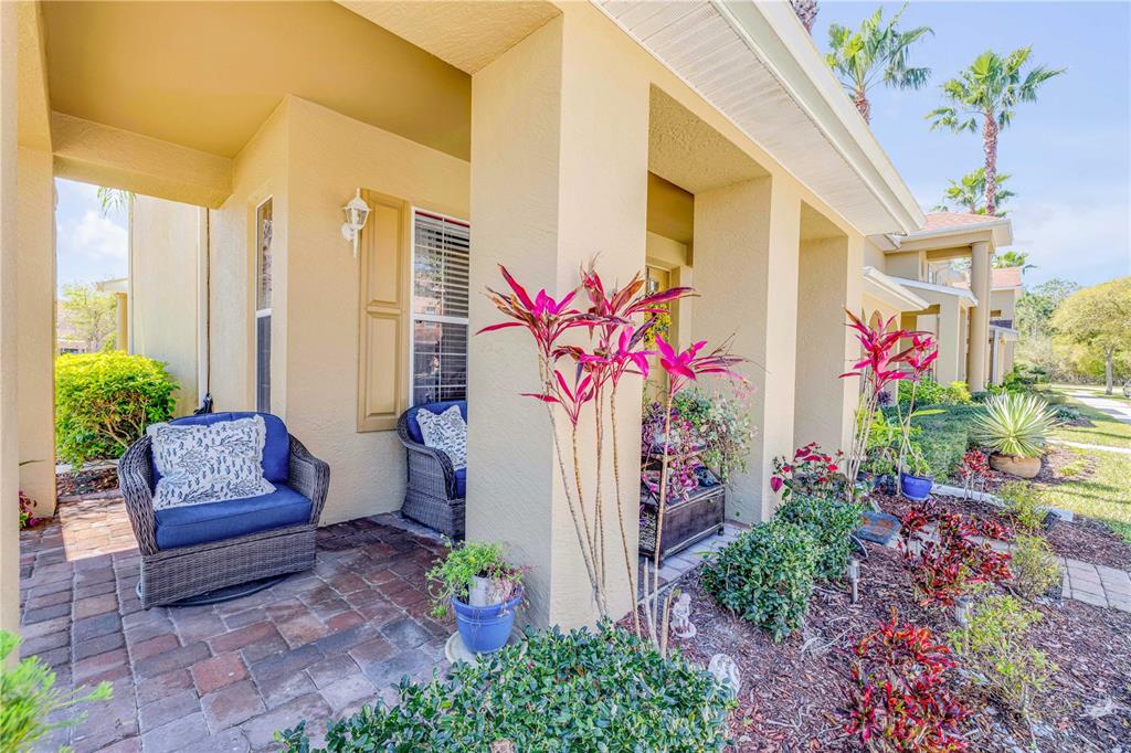 A covered front porch features brick pavers, two wicker chairs, and various potted plants — 3621 CASELLO DRIVE, NEW SMYRNA BEACH, FL
