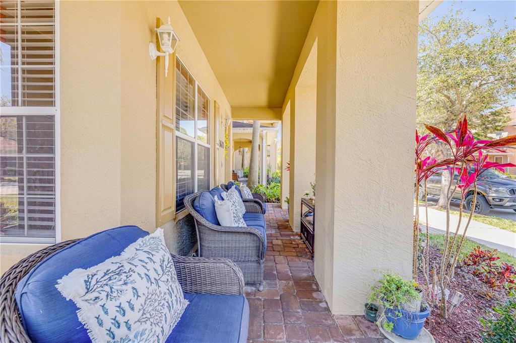 A covered front porch features brick pavers, wicker furniture with blue cushions, and a window — 3621 CASELLO DRIVE, NEW SMYRNA BEACH, FL