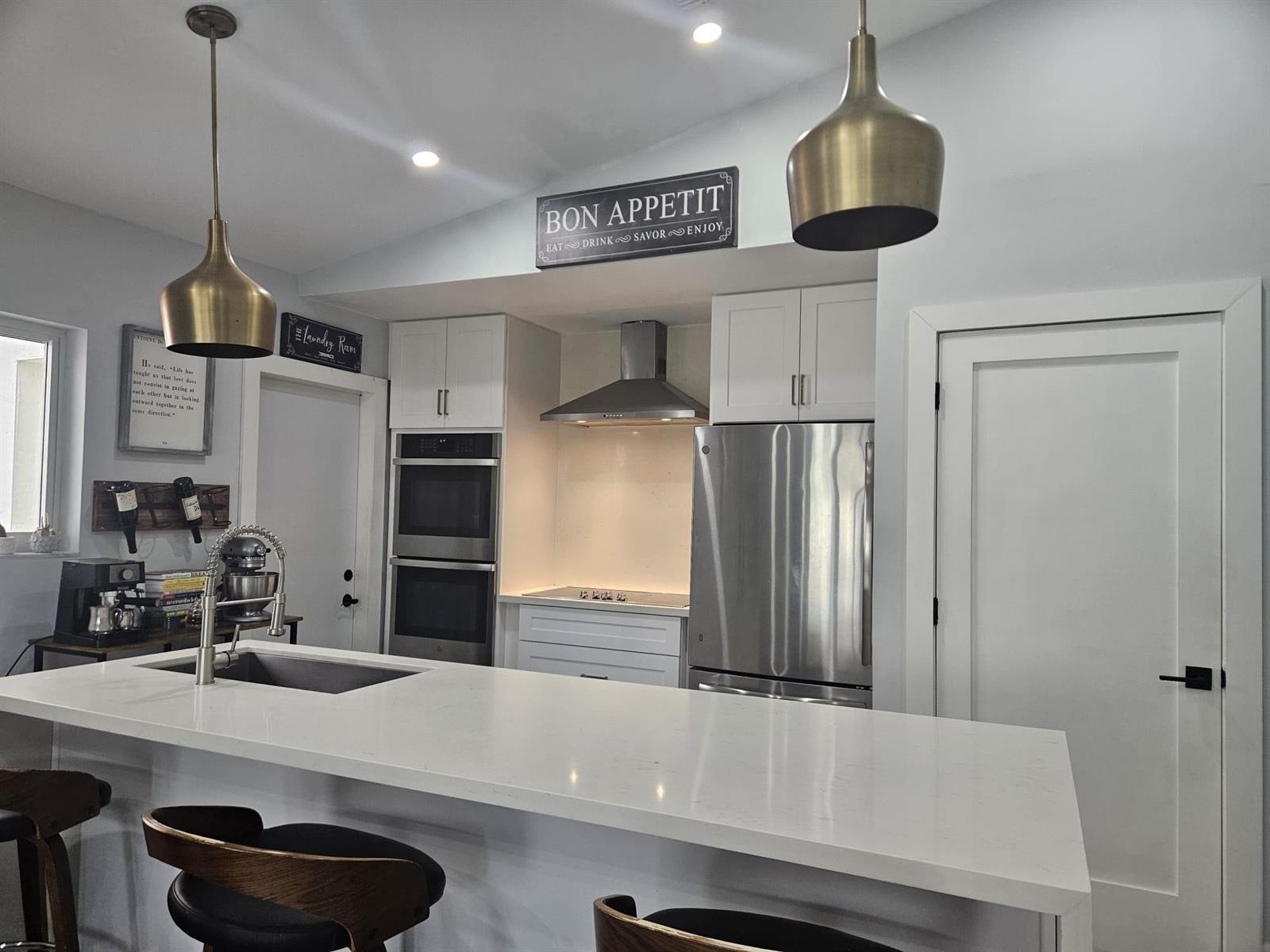A modern kitchen features white cabinetry, stainless steel appliances, a quartz island, and pendant lighting — 16218 SW 100th Terrace # 16218, Miami FL 33196, MIAMI, FL