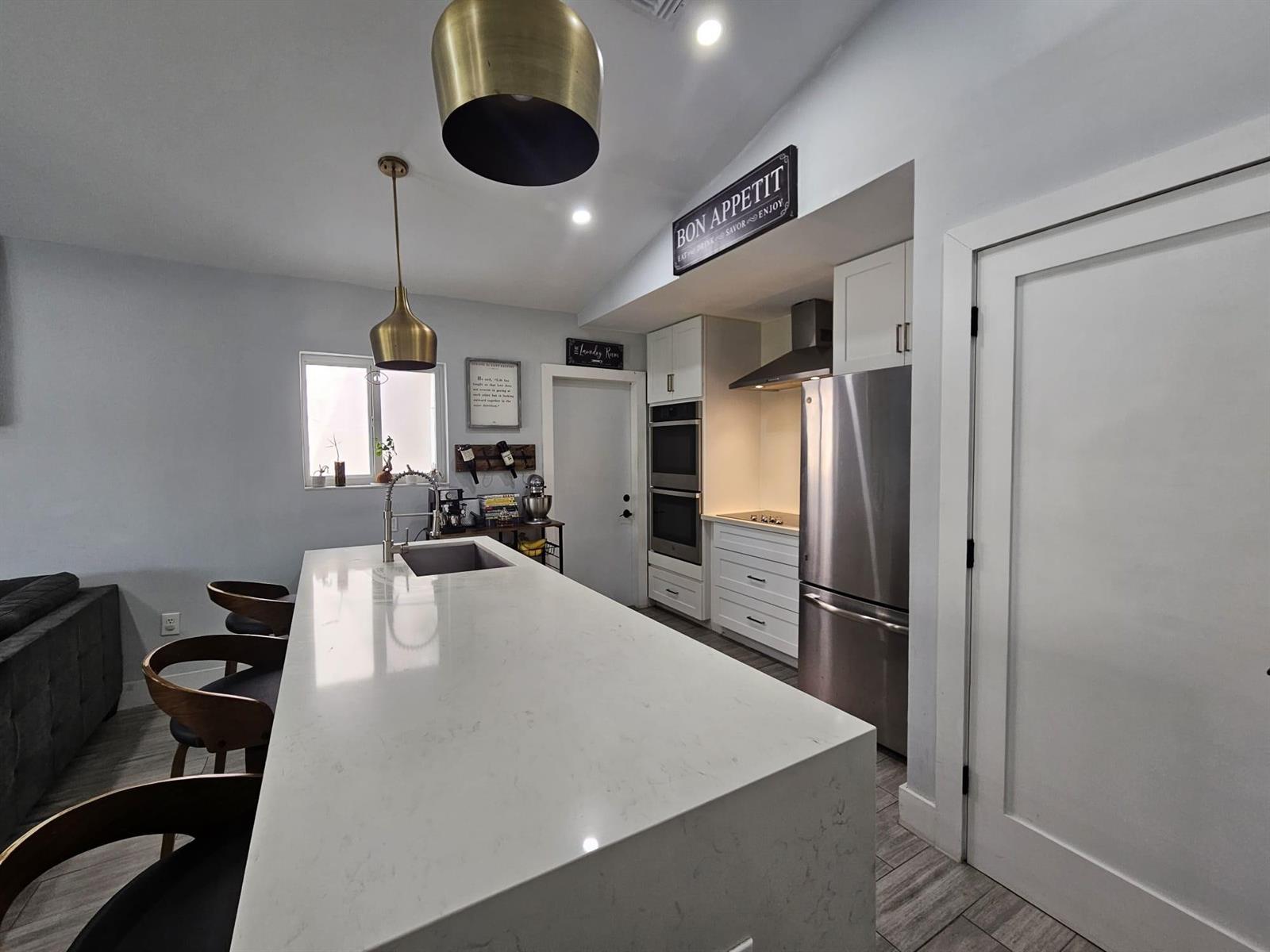 A modern kitchen features a large white quartz island, stainless steel appliances, and brass pendant lights — 16218 SW 100th Terrace # 16218, Miami FL 33196, MIAMI, FL