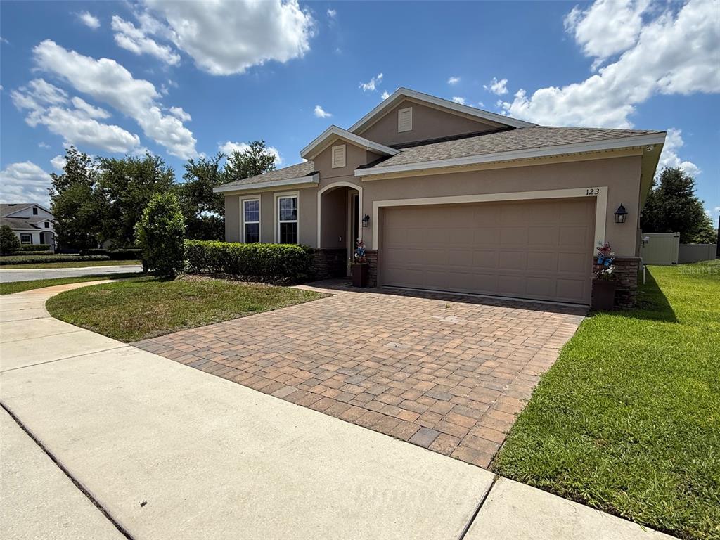 A tan single-story house features a paver driveway, a two-car garage, and a landscaped yard — 123 GREEN BRANCH BOULEVARD, GROVELAND, FL